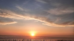 Ein Sonnenuntergang über dem Meer mit einem hölzernen Steg im Vordergrund.