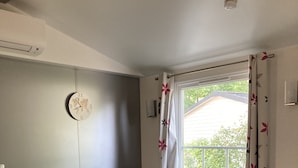 Ein Zimmer mit einem blauen Ecksofa, einem weißen Tisch, einer Uhr und einem Fenster mit Vorhängen.
