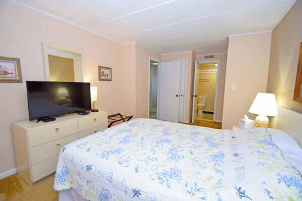 A hotel room with a bed, a TV on a dresser, a mirror, and a door leading to a bathroom.