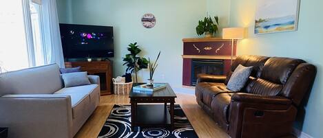 A living room with a sofa, a leather armchair, a coffee table, a TV, a fireplace, and a ceiling fan.