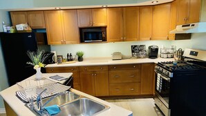 A modern kitchen with wooden cabinets, a stainless steel sink, a microwave, a stove, and a coffee maker. - KingBed,Sleeps10+,SmrtTV,BBQ,Gym,FireTable,FullKitchen. All in walking distance. (Goderich)