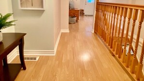 A hallway with wooden flooring, a staircase with a wooden railing, and a framed artwork on the wall. - KingBed,Sleeps10+,SmrtTV,BBQ,Gym,FireTable,FullKitchen. All in walking distance. (Goderich)