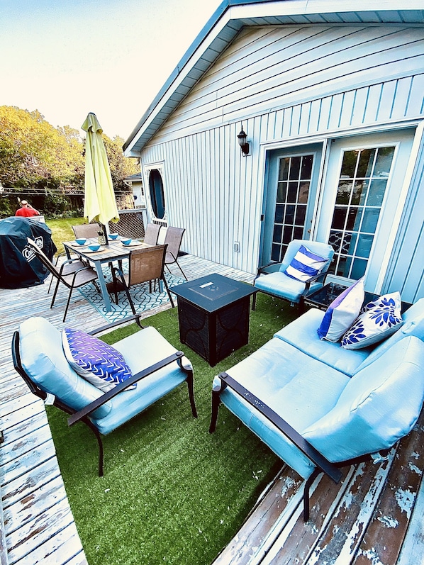 Una terraza con mobiliario exterior, una mesa y una parrilla.
