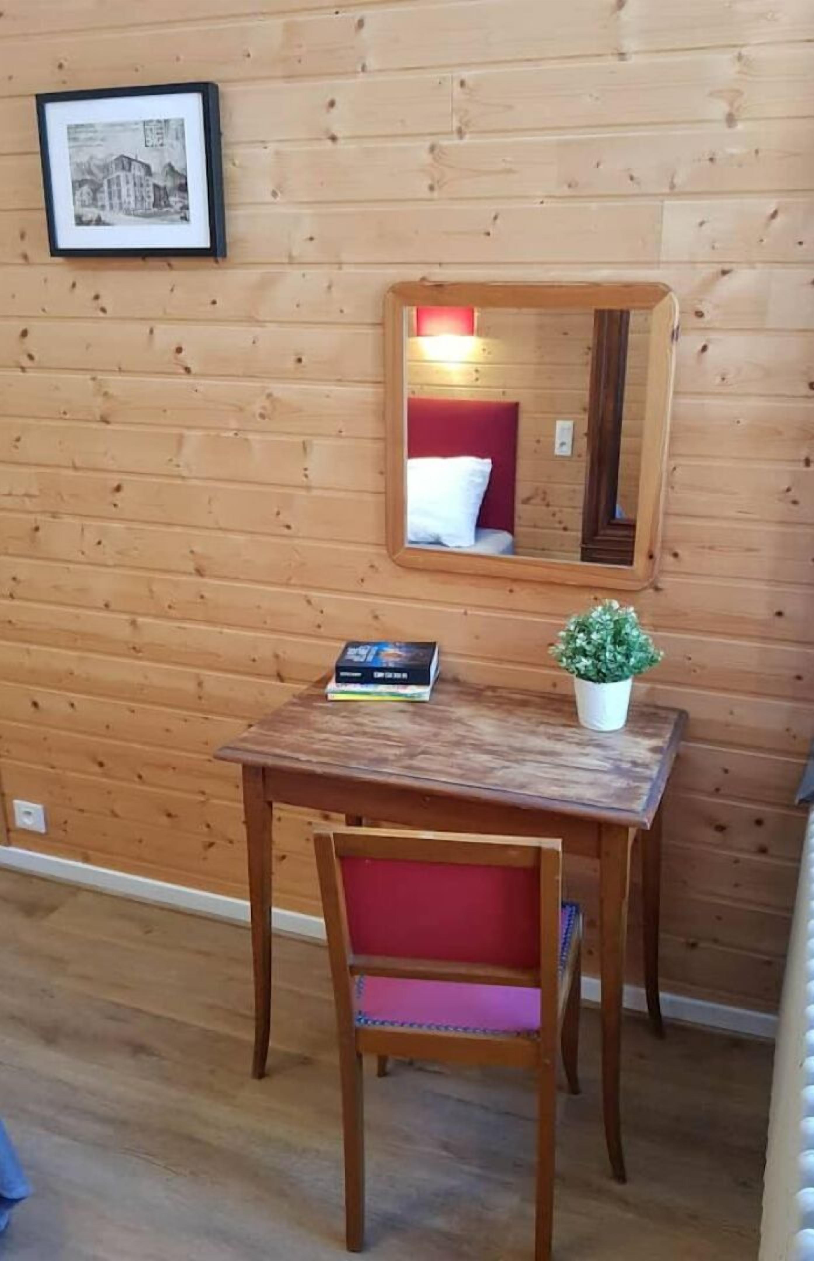 Una habitación con paneles de madera, una pequeña mesa, una silla, un cuadro enmarcado y un espejo en la pared.