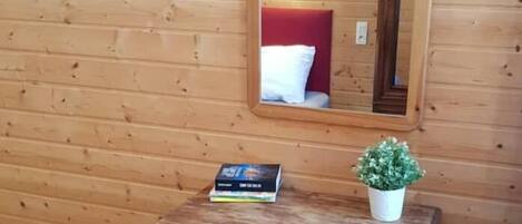 Una habitación con paneles de madera, una pequeña mesa, una silla, un cuadro enmarcado y un espejo en la pared.