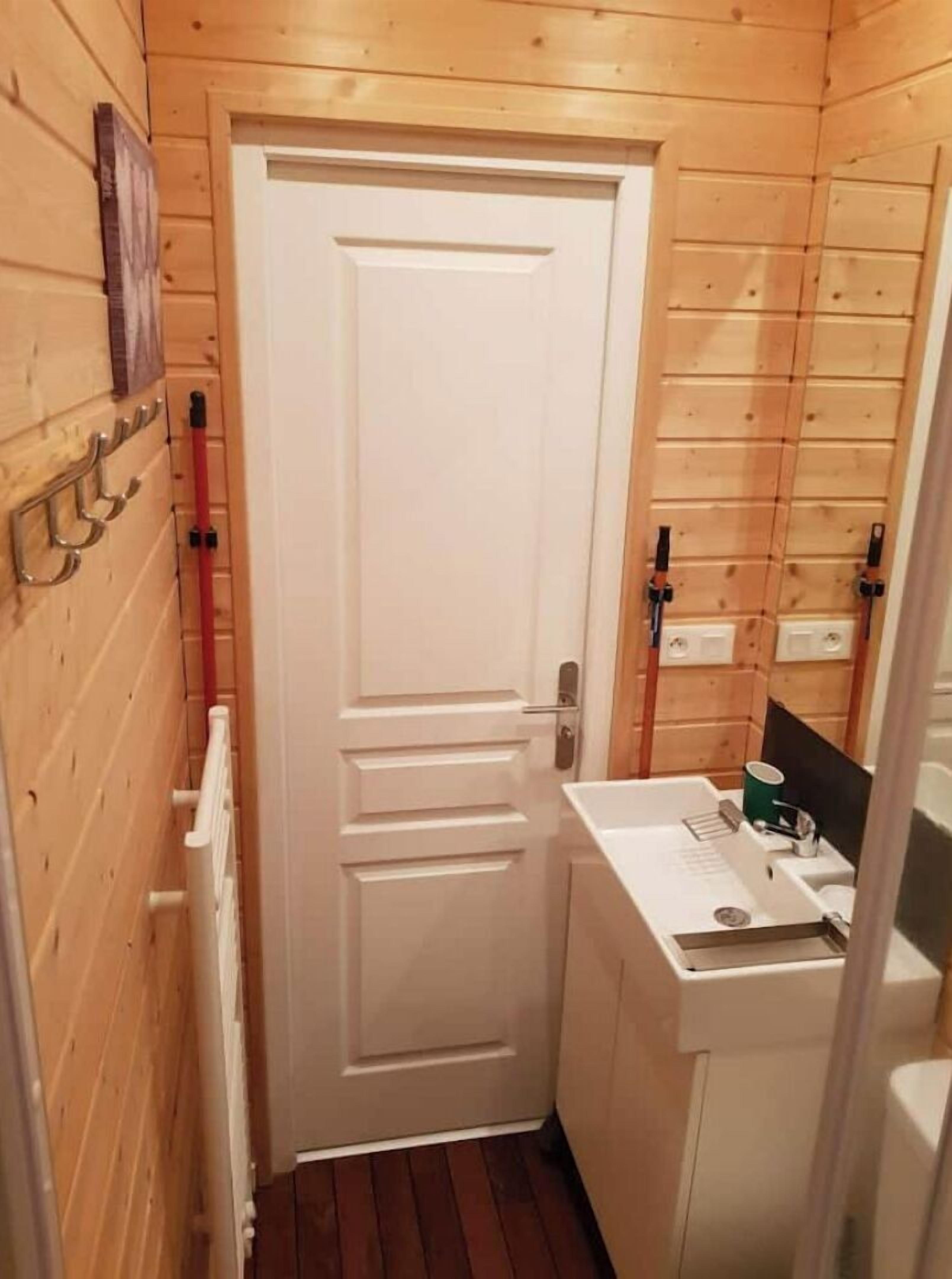 Un baño pequeño y acogedor con paredes de madera, una puerta blanca y un lavamanos blanco con un espejo encima.