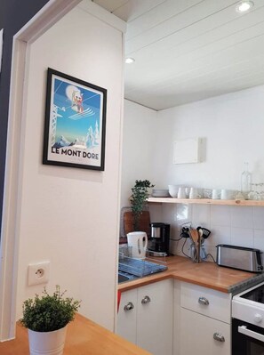 Una cocina compacta con armarios blancos, encimera de madera, una cafetera y una pequeña planta en maceta.