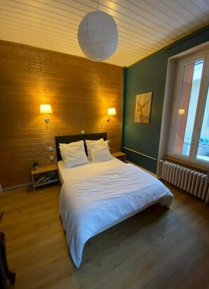 Une chambre avec un plancher en bois, un lit avec une literie blanche, deux lampes de chevet et une grande fenêtre donnant sur un beau paysage.