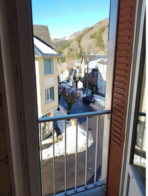 A view from a balcony with a metal railing, overlooking a residential street with houses and a snow-covered ground. - Apartment N°04 "Pas de l'Âne" 4 people (Mont-Dore)