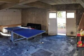 Una habitación con mesa de ping pong, una silla y una mesa con objetos encima.