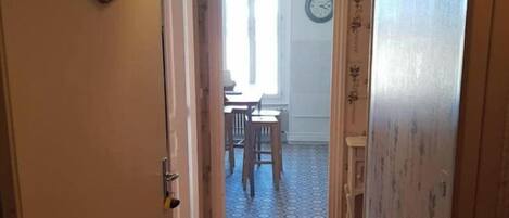 Un pasillo estrecho con piso de madera que lleva a un comedor con una mesa y sillas.