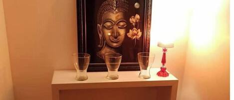 Eine gerahmte Buddha-Statue auf einem weißen Konsolentisch mit drei klaren Gläsern und einer roten Lampe.