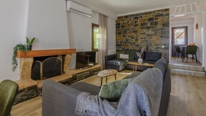 A modern living room with a stone fireplace, a grey sofa, a TV, and a dining area with a table and chairs. - Nami Villa Beach Front Airport by Airstay (Spata-Artemida)