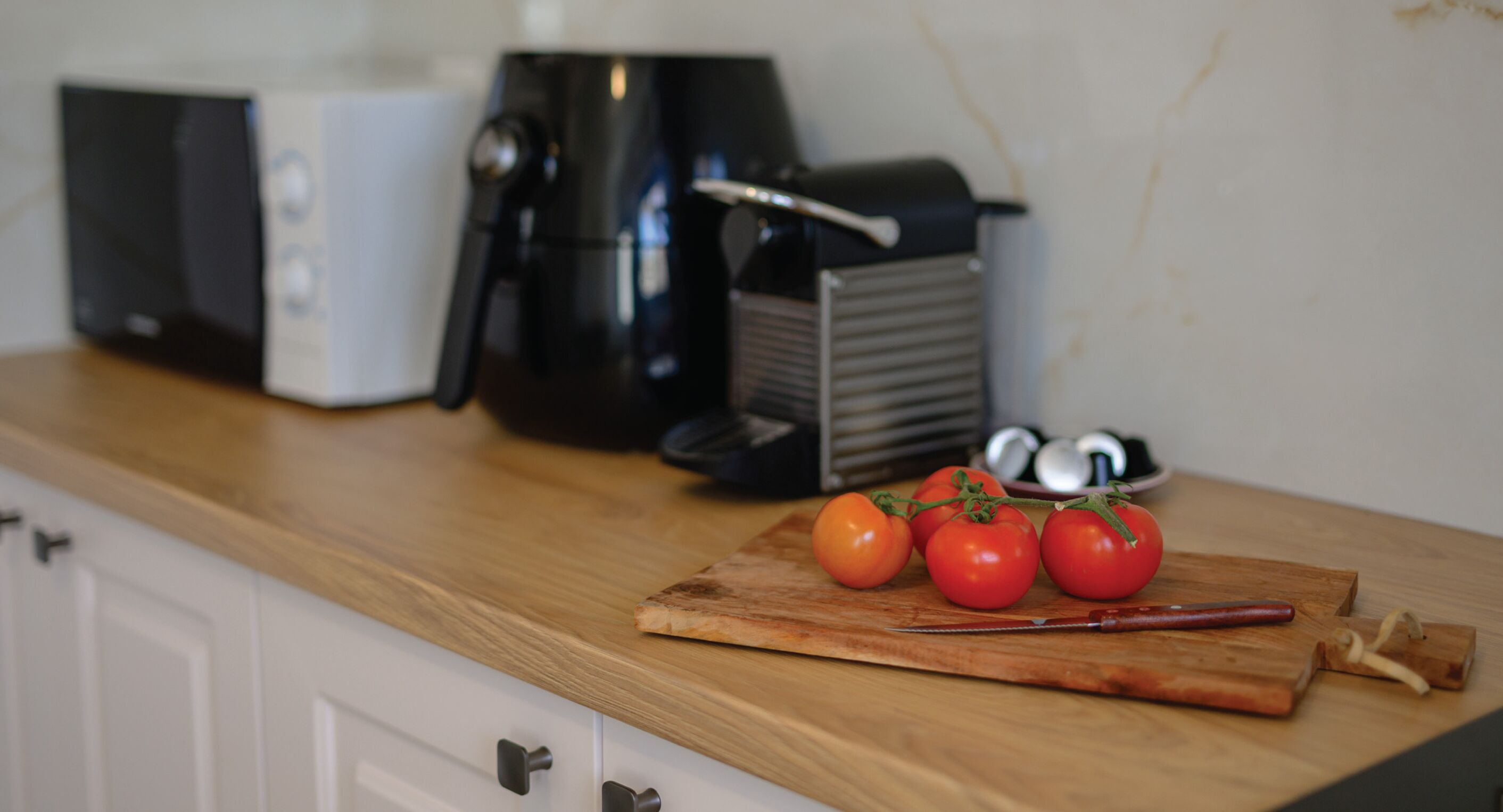A kitchen counter with a coffee maker, a toaster, and a cutting board with tomatoes and a knife.