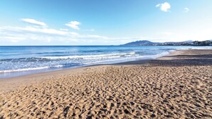 A wide sandy beach with gentle waves, a clear sky, and distant mountains. - Nami Villa Beach Front Airport by Airstay (Spata-Artemida)