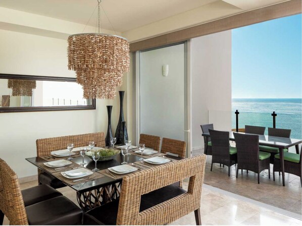 A dining area with a table set for four, a wicker chair, and a view of the ocean.