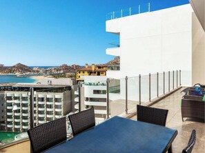A balcony with a table and chairs, overlooking a beach and buildings.