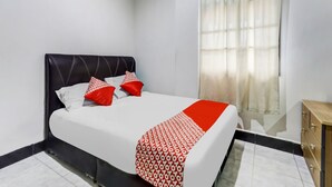 Un lit bien fait, recouvert d’une couverture à motifs blancs et rouges, avec une tête de lit noire et deux oreillers rouges.