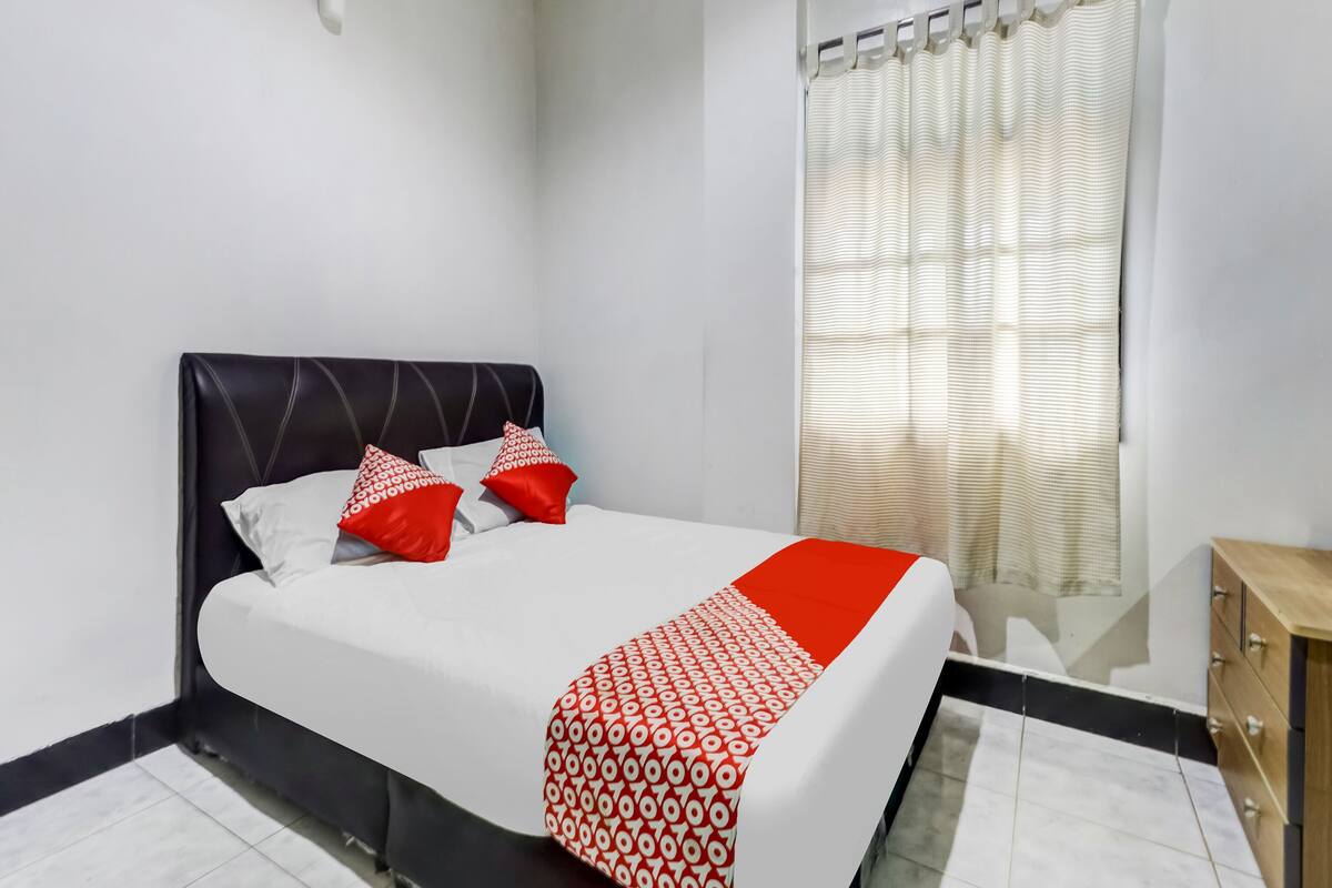 A neatly made bed with a white and red patterned blanket, a black headboard, and two red pillows.