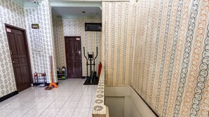 Un couloir avec un papier peint à motifs, une porte, une petite étagère avec quelques objets et un escalier.