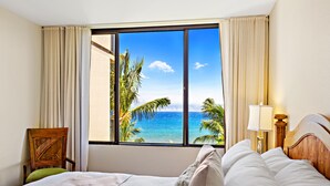 Une chambre d’hôtel dotée d’une grande fenêtre donnant sur l’océan et les palmiers.