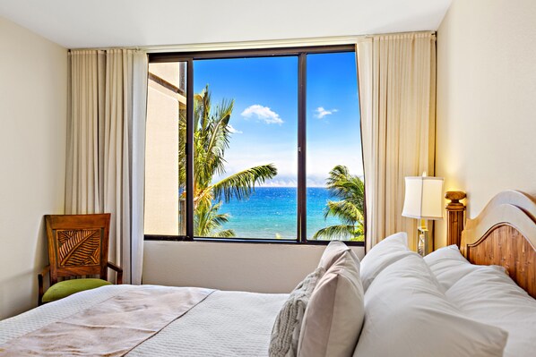 Una habitación de hotel con un ventanal que ofrece vista al océano y palmeras.