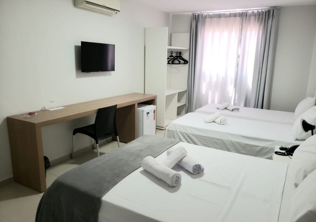 A hotel room with a desk, two beds, a TV, and a wardrobe.