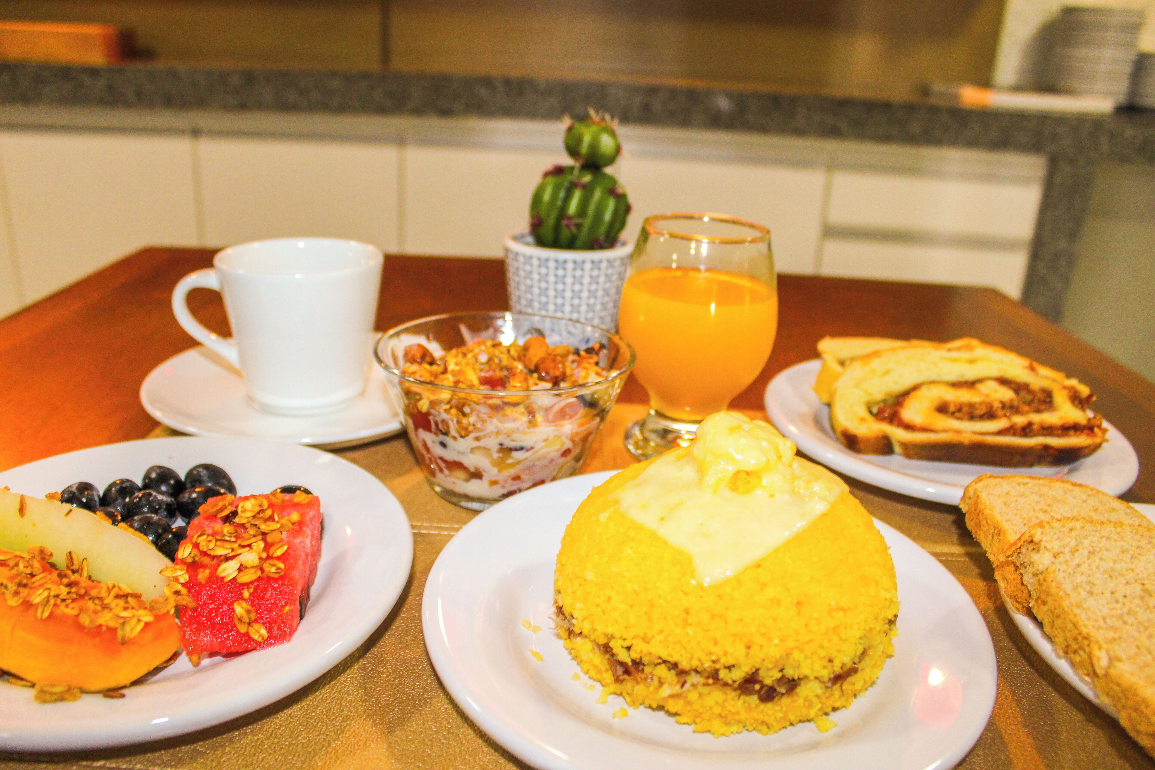 Une table de petit-déjeuner avec des assiettes remplies de nourriture, une tasse, un verre de jus d’orange et une petite décoration en forme de cactus.