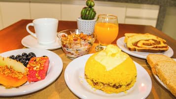 Une table de petit-déjeuner avec des assiettes remplies de nourriture, une tasse, un verre de jus d’orange et une petite décoration en forme de cactus.