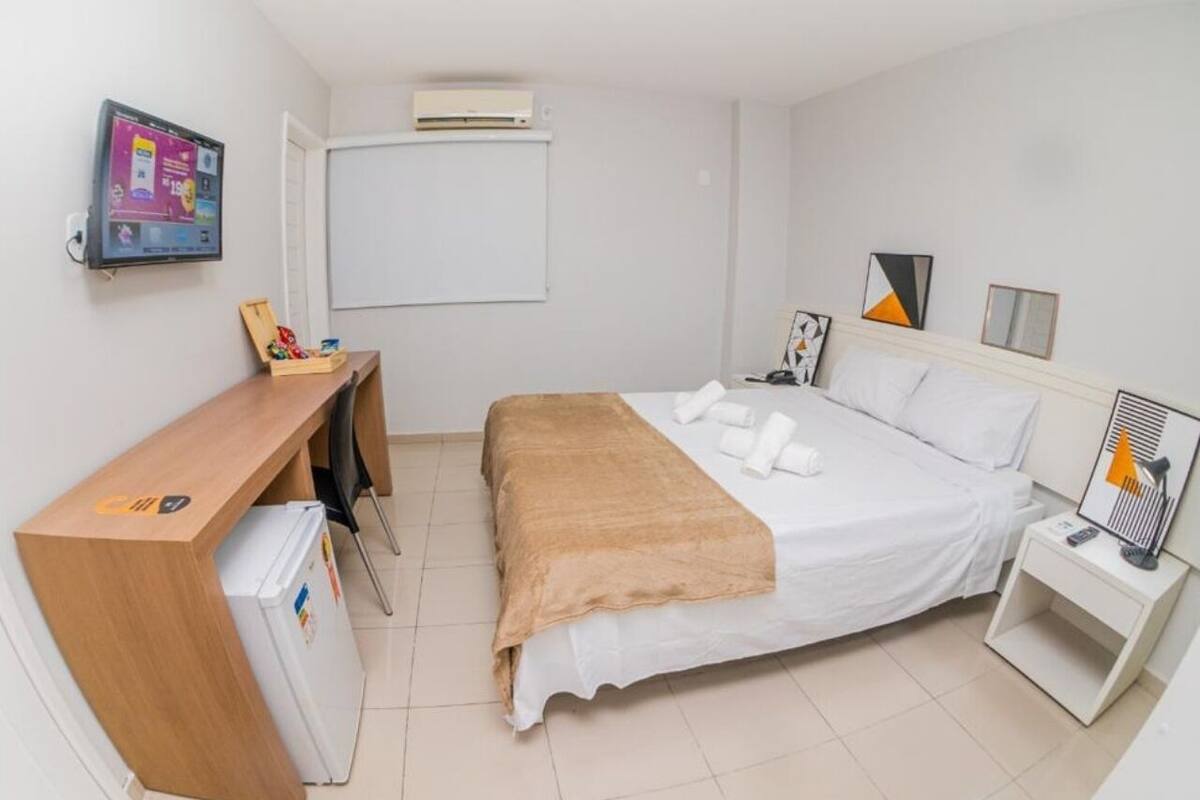 Ein Hotelzimmer mit einem Bett, einem Schreibtisch, einem Sessel, einem kleinen Kühlschrank, einem Fernseher und einem Nachttisch mit Lampe.