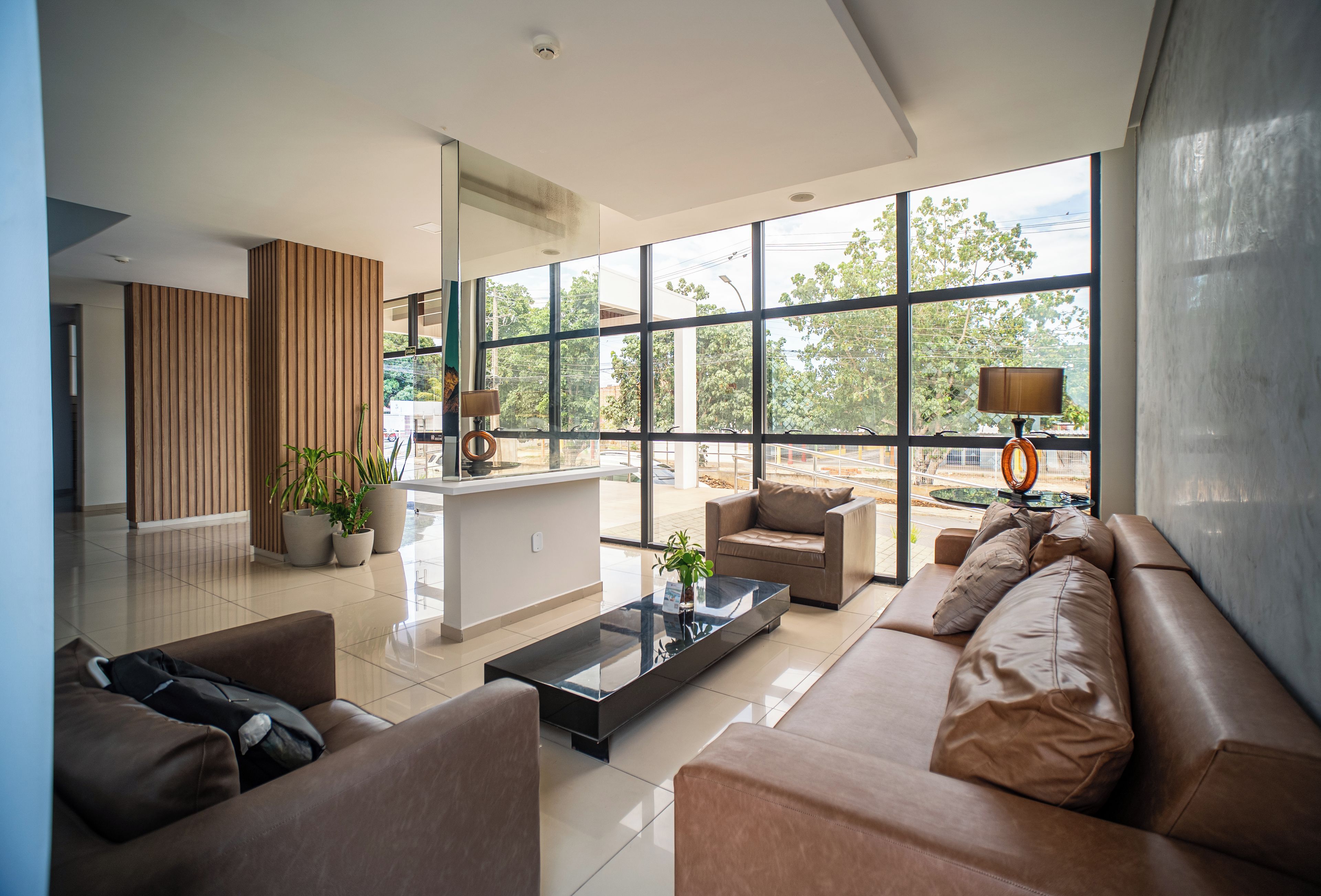A modern living room with a sofa, armchairs, a coffee table, and a large window with a view of trees and buildings.