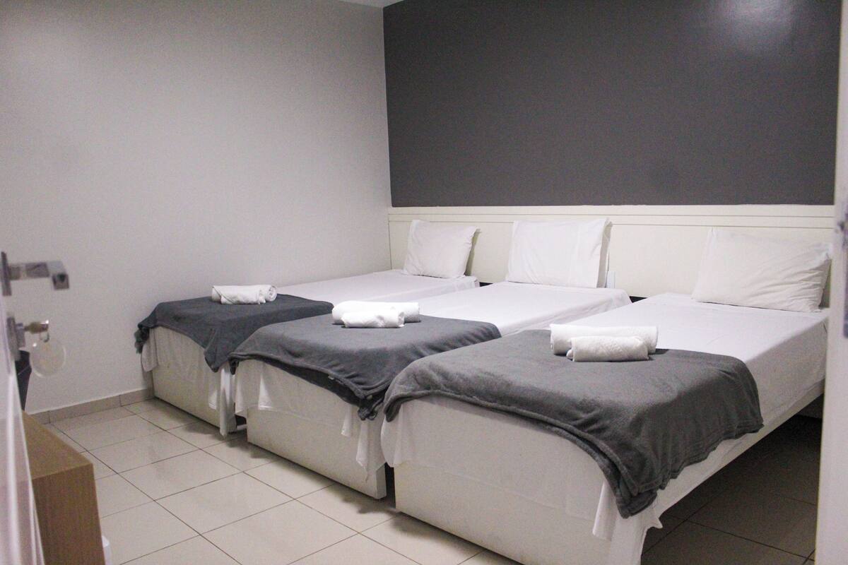 Ein Hotelzimmer mit zwei Einzelbetten, jeweils mit grauer Decke und weißen Kissen.