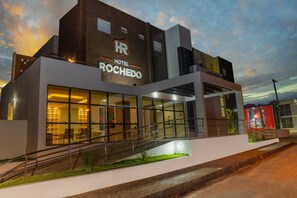 A modern hotel with a prominent 'Hotel Rochero' sign, large glass windows, and a staircase leading to the entrance. - HOTEL ROCHEDO (Penedo)