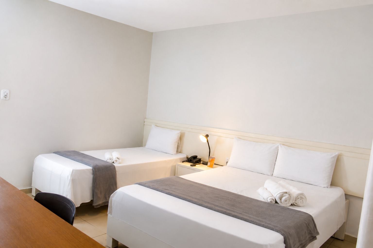 Een hotelkamer met twee enkele bedden, een bureau, een stoel, een nachtkastje met een lamp en een telefoon.