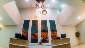 A reception area with a curved desk, a large wall-mounted screen displaying a mountain landscape, and a modern ceiling design with recessed lighting. - HOTEL ROCHEDO (Penedo)