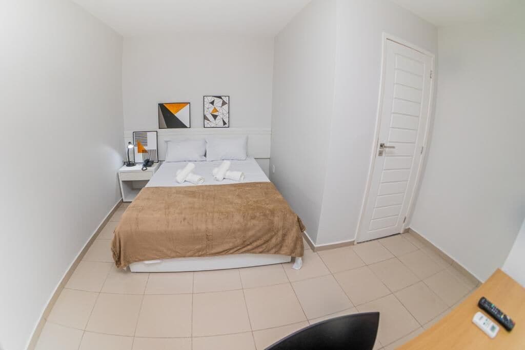 A hotel room with a bed, a nightstand, a desk, and a door.