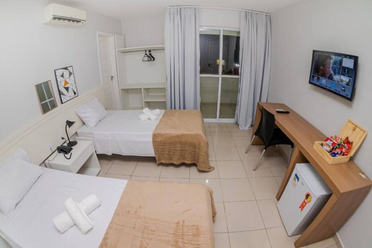 Ein Hotelzimmer mit zwei Betten, einem Schreibtisch, einem Fernseher und einer Schiebetür zum Balkon.