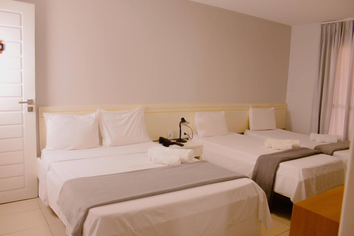 Ein Hotelzimmer mit zwei Betten, einem Nachttisch, einer Lampe und einem Fenster mit Vorhängen.