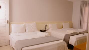 A hotel room with two beds, a bedside table, a lamp, and a window with curtains.