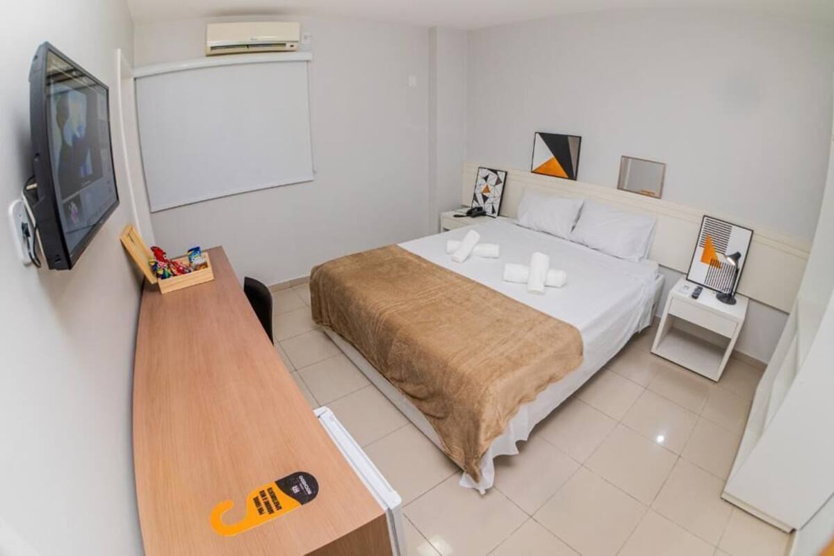 Ein Hotelzimmer mit Bett, Schreibtisch, Fernseher und Nachttisch mit Lampe.