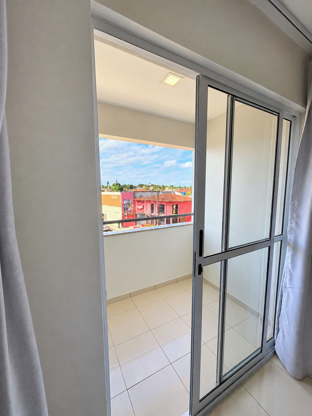 Ein Zimmer mit einer Schiebetür zu einem Balkon mit Blick auf Gebäude und einen klaren Himmel.