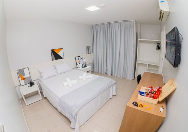 Une chambre d’hôtel avec un lit, une table de chevet avec une lampe, une télévision, une armoire et une petite table en bois avec des collations.