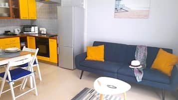 Un espacio habitable compacto con kitchenette, comedor y sofá con cojines.