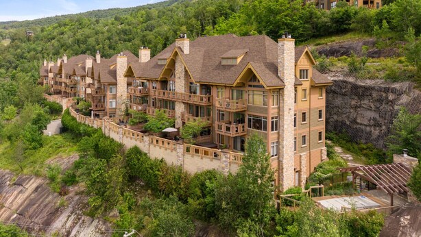 Un bâtiment à plusieurs étages, de style chalet, avec une façade en pierre, de nombreux balcons et un paysage naturel environnant.