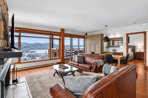 A spacious living room with a large window, leather sofas, a glass coffee table, and a fireplace. - Tremblant Prestige - Altitude 172-8 (Mont-Tremblant)