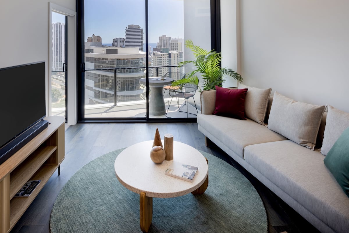 A modern living room with a large TV, a round coffee table, a sofa, and a balcony with a city view.