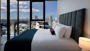 A modern hotel room with a large bed, a city view, and a city skyline visible through the windows.