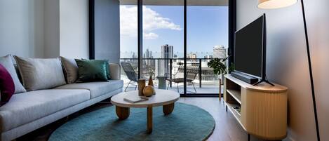 A modern living room with a sofa, a coffee table, a TV on a stand, and a large window with a city view.