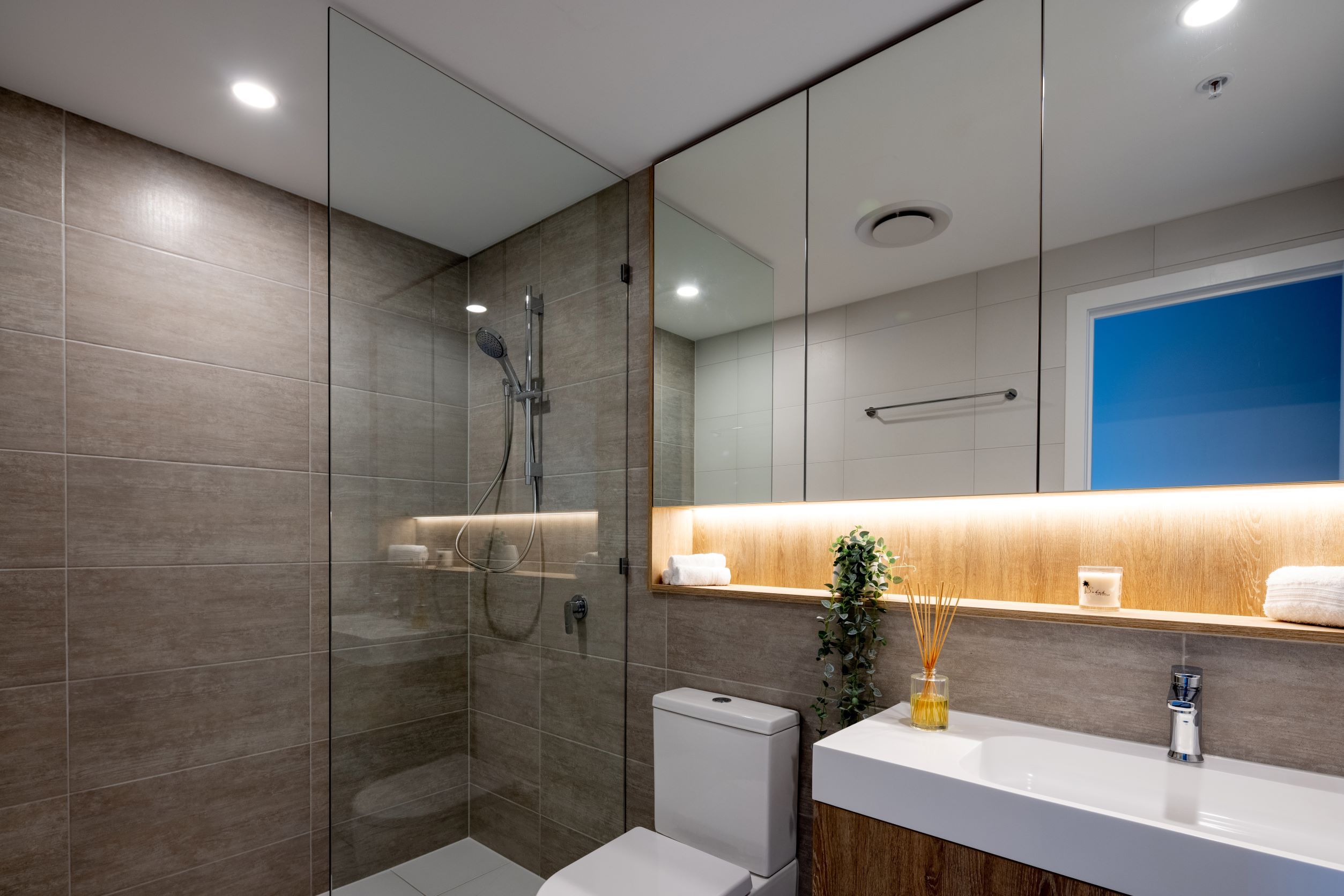 A modern bathroom with a glass-enclosed shower, a white toilet, a sink with a wooden countertop, and a mirror above the sink.