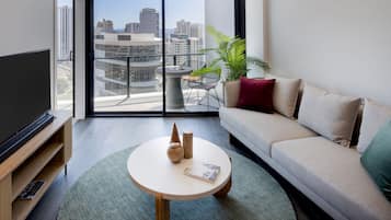 A modern living room with a large TV, a round coffee table, a sofa, and a balcony with a city view.